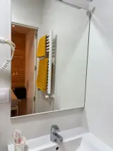 Ducha con toalla gris en el plato, inodoro y lavabo junto a la ventana del baño
